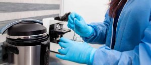 Experto en inmunohistoquímica manipulado instrumentos para realizar estudios, se encuentra en un laboratorio y viste con guantes de látex azules y bata azul.